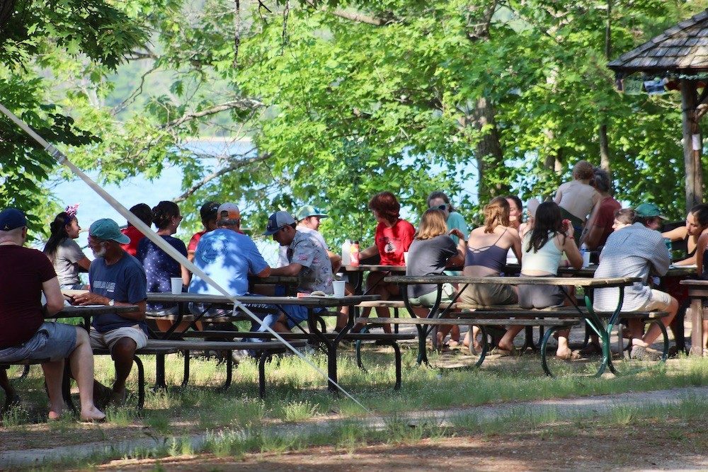 People eating at picnic tables along lake