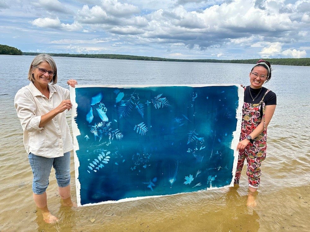 Two women standing in water holding a piece of art outside