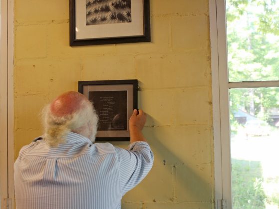 A man hangs a framed poem on a wall.