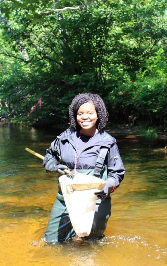 A student holds a net while standing in a stream.
