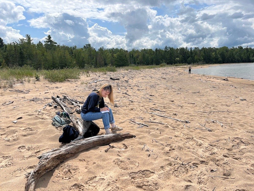 Student sitting on a beach and writing in her notebook